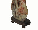 An intricately carved stone sculpture depicting a scenic landscape, mounted on a dark brown wooden display stand against a plain white background.