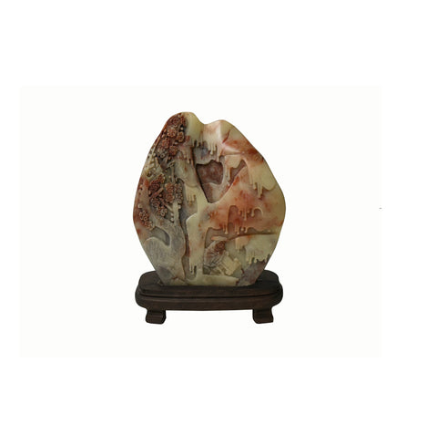 A carved decorative stone sculpture with a landscape motif, displayed on a dark wooden stand against a plain white background.