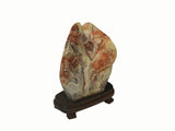 A carved decorative stone sculpture with a landscape motif, displayed on a dark wooden stand against a plain white background.