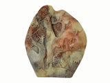 A carved stone plaque featuring a detailed landscape scene with trees, mountains, and a figure, crafted from marbled stone in cream, brown, and reddish tones on a plain white background.